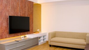 Ett modernt vardagsrum med en platt-TV som är monterad på en träpanel, en beige soffa och ett trägolv.