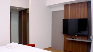 Ett hotellrum med en säng, en tv som är monterad på väggen, en garderob i trä och en röd stol.
