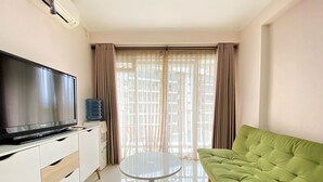 A living room with a flat-screen TV, a water dispenser, a round glass table, and a green sofa. - Homey And Cozy 2Br At Gateway Pasteur Apartment (Cimahi)