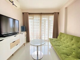 Una sala de estar con una televisión de pantalla plana, un dispensador de agua, una mesa redonda de vidrio y un sofá verde.
