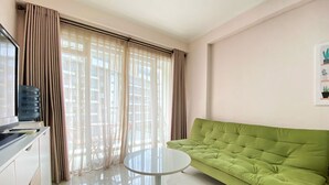 A modern living room with a green sofa, a small round table, and a large window with curtains. - Homey And Cozy 2Br At Gateway Pasteur Apartment (Cimahi)