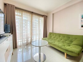A modern living room with a green sofa, a small round table, and a large window with curtains.