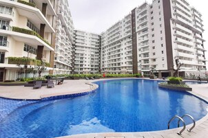 Un moderno edificio residencial con piscina central, balcones con vegetación y un área exterior bien cuidada.