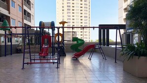 Ein Spielplatz im Freien mit Rutschen und Klettergerüsten, umgeben von Hochhäusern.