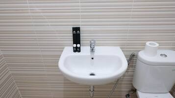 A bathroom with a white sink, a toilet, and a towel dispenser.
