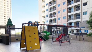 Ein Spielplatz im Freien mit einer gelben Kletterattrappe, einer grünen Rutsche und einer roten Schaukel.