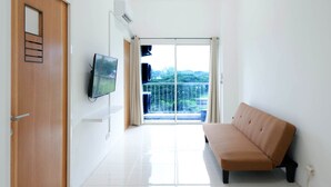 Ein modernes Zimmer mit einer Schiebeglastür, die auf einen Balkon führt, einem wandmontierten Flachbildfernseher und einem beigefarbenen Sofa.
