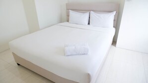 Ein ordentlich bezogenes Bett mit weißen Leinen und einem gefalteten weißen Handtuch, ein Kopfteil mit zwei Kissen und eine schlichte weiße Wand.