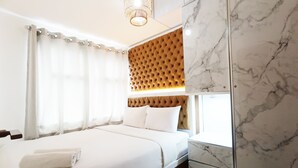 A modern hotel room with a large bed, a tufted headboard, a marble wall, and a hanging light fixture. - Comfort 2Br At 28Th Floor Vida View Makassar Apartment (Makassar)