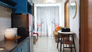 A compact kitchen with modern appliances, a dining area with a small table and chairs, and a view of a room with a curtain featuring a Union Jack design. - Comfort 2Br At 28Th Floor Vida View Makassar Apartment (Makassar)