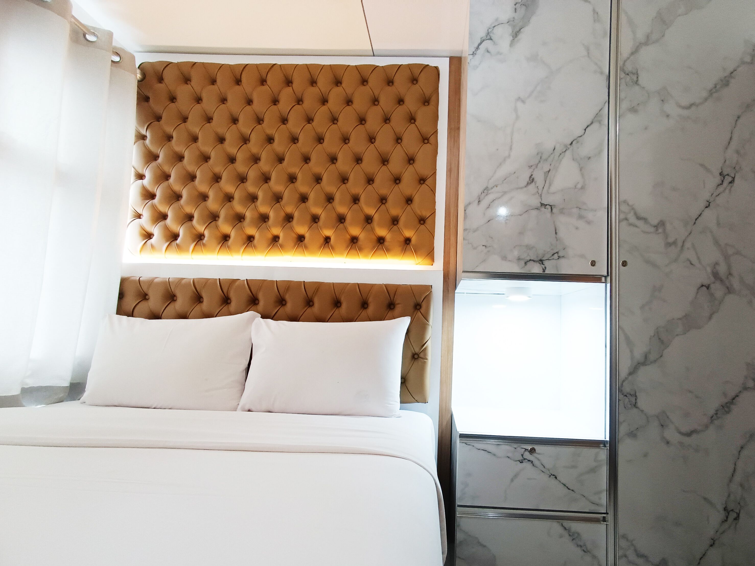 A bedroom with a tufted headboard, white bedding, and marble walls.