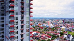 A high-rise building with multiple balconies, a cityscape in the background, and a mix of residential and commercial buildings. - Comfort 2Br At 28Th Floor Vida View Makassar Apartment (Makassar)