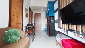 A modern kitchen with a large flat-screen TV, wooden cabinets, and a dining area with chairs and a table. - Comfort 2Br At 28Th Floor Vida View Makassar Apartment (Makassar)