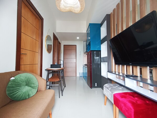 A modern kitchen with a large flat-screen TV, wooden cabinets, and a dining area with chairs and a table.