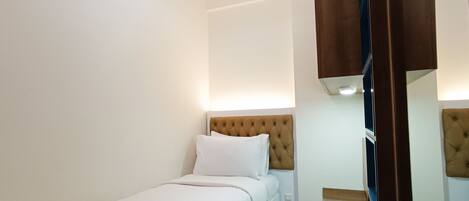 A neatly made bed with white linens and a single pillow, a bedside table, and a wall-mounted light fixture.