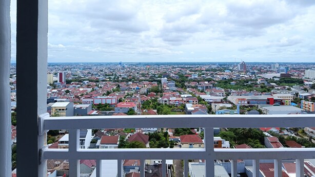 A cityscape viewed from a balcony with a white railing. - Comfort 2Br At 28Th Floor Vida View Makassar Apartment (Makassar)