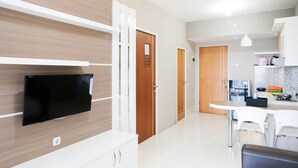 A modern kitchen with white cabinets, a black flat-screen TV mounted on the wall, and a dining area with white chairs and a round table. - Homey 2Br At Puncak Bukit Golf Surabaya Apartment (Surabaya)