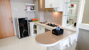 A compact kitchen with a refrigerator, a stove, a sink, and a small dining area with a table and chairs. - Homey 2Br At Puncak Bukit Golf Surabaya Apartment (Surabaya)