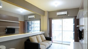 A modern hotel room with a sofa, a TV, air conditioning units, and a large window with curtains. - Homey 2Br At Puncak Bukit Golf Surabaya Apartment (Surabaya)