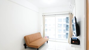 A minimalist living room with a sofa, a TV mounted on the wall, and a window with a view of buildings. - Spacious And Best Deal 2Br Apartment At Puncak Bukit Golf Surabaya (Surabaya)