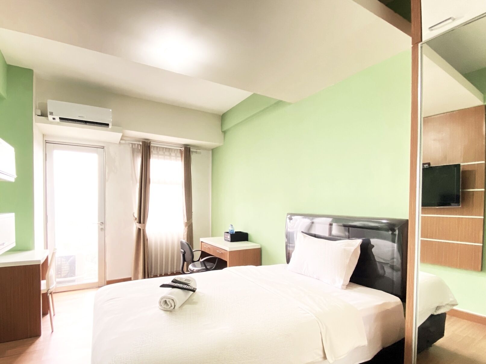 Une chambre d’hôtel équipée d’un lit, d’un bureau, d’un climatiseur, d’une télévision et d’une porte avec des rideaux.
