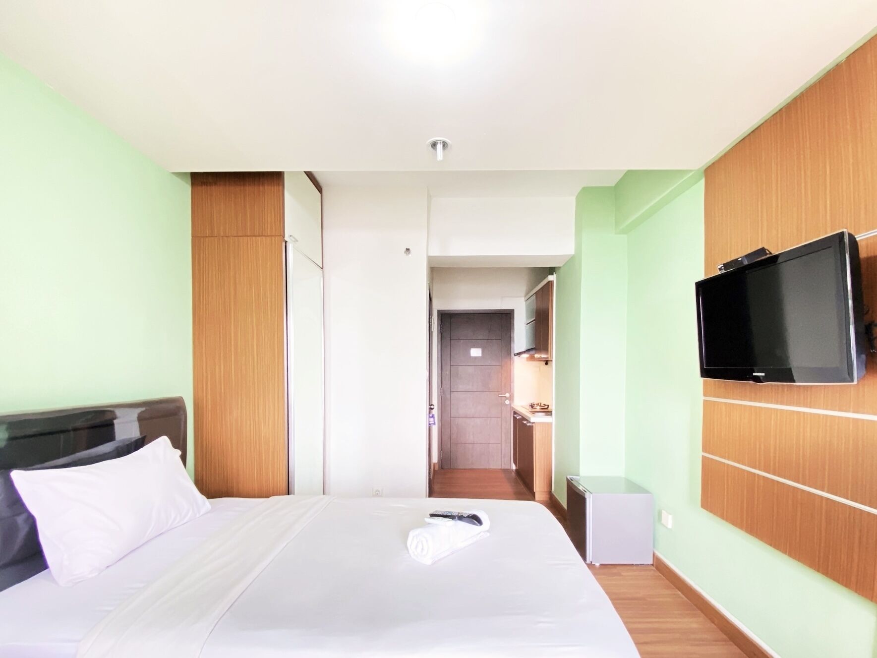 Een hotelkamer met een bed, een aan de muur bevestigde televisie en een kitchenette.