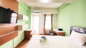 A hotel room with a bed, a TV, a desk, a chair, and a window with curtains.