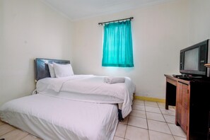 A room with a bed, a television on a wooden cabinet, and a teal curtain.