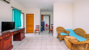 Een woonkamer met een televisie, houten meubels, rieten stoelen en een bank.