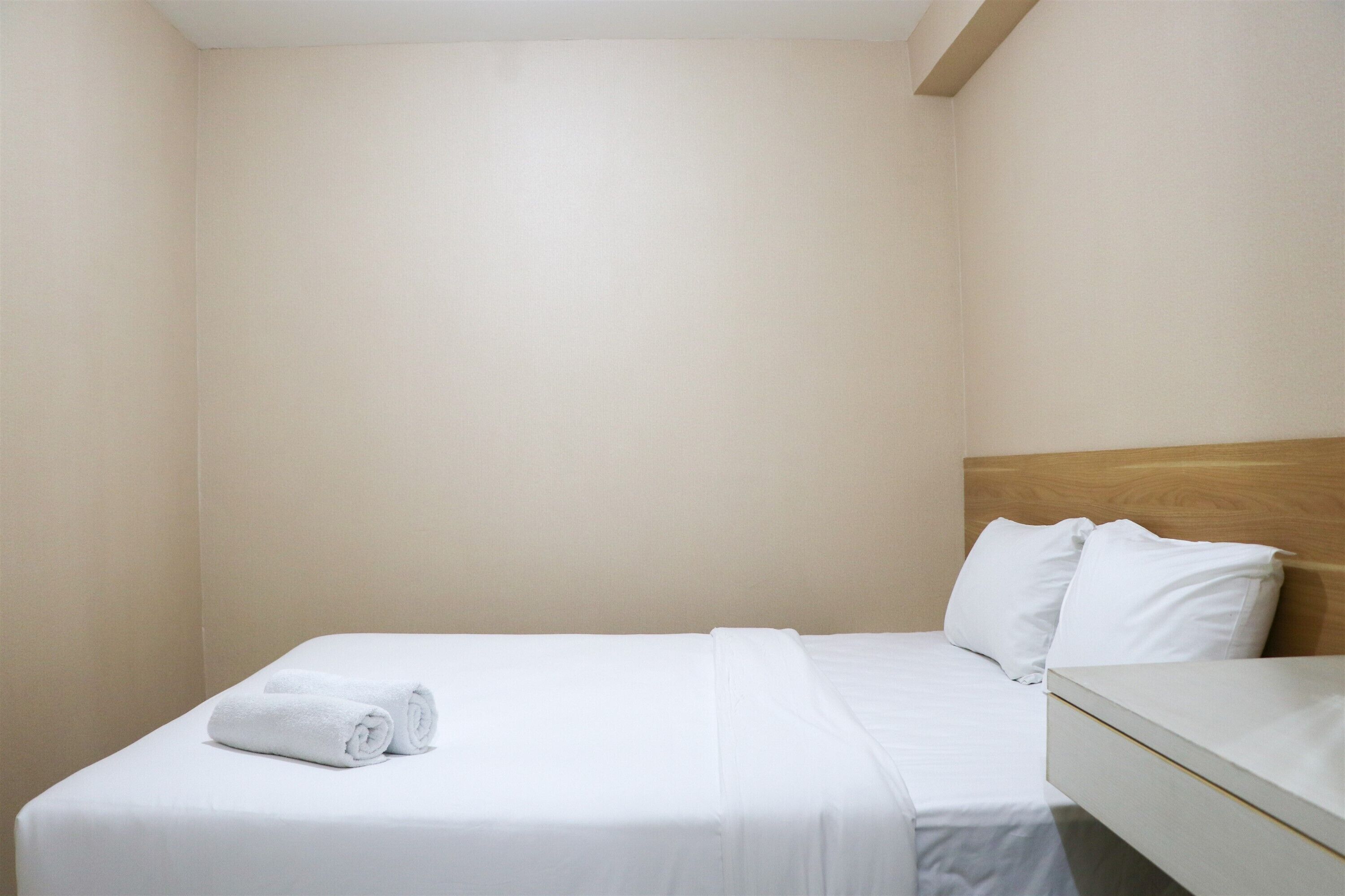 A neatly made bed with white linens and pillows, a wooden headboard, and a white bedside table.