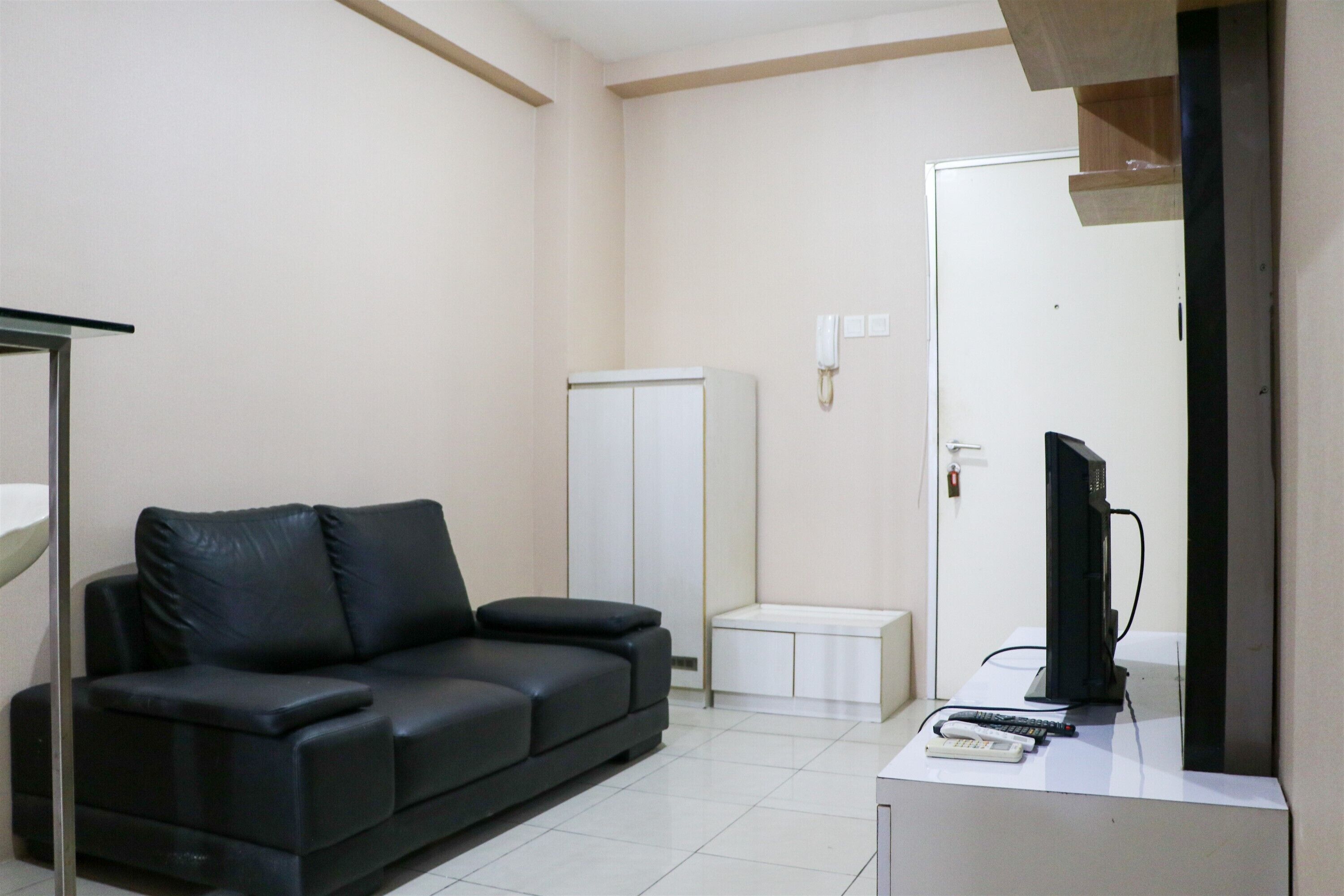 A modern living room with a black leather sofa, a small white cabinet, a television on a stand, and a telephone on the wall.