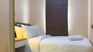 A neatly made bed with white linens and pillows, a wooden headboard, and a small bedside table with a book. - Cozy Living And Tidy 2Br Green Bay Pluit Apartment (Jakarta)