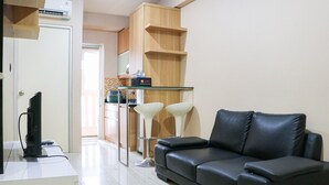 A modern living room with a black leather sofa, a glass coffee table, and two white bar stools. - Cozy Living And Tidy 2Br Green Bay Pluit Apartment (Jakarta)