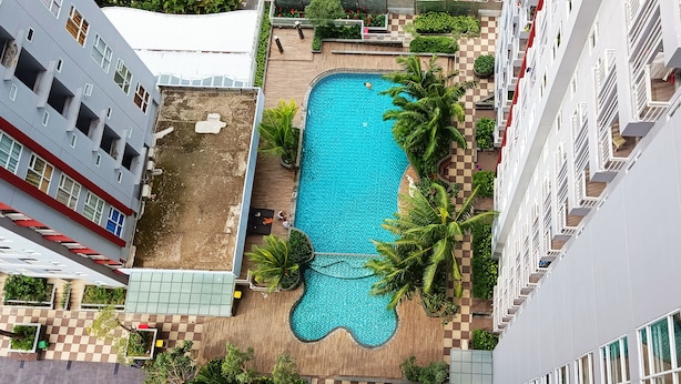 Vista aérea de un edificio residencial con piscina rodeada de palmeras y un sendero con diseño de cuadros.