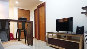 Una sala de estar moderna con un sofá, un televisor sobre un mueble de madera, un comedor con mesa y sillas, y una cocina con un cilindro de gas.