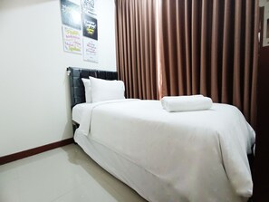 A neatly made bed with white linens, a dark headboard, and a brown curtain in a hotel room. - Luxury 2Br At Vida View Makassar Apartment (Makassar)