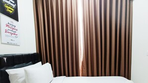 Una habitación de hotel con cama, almohadas blancas, cabecero negro y cortinas marrones.