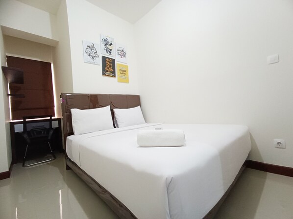 A neatly made bed in a hotel room with a clean, white wall and a small desk area. - Luxury 2Br At Vida View Makassar Apartment (Makassar)