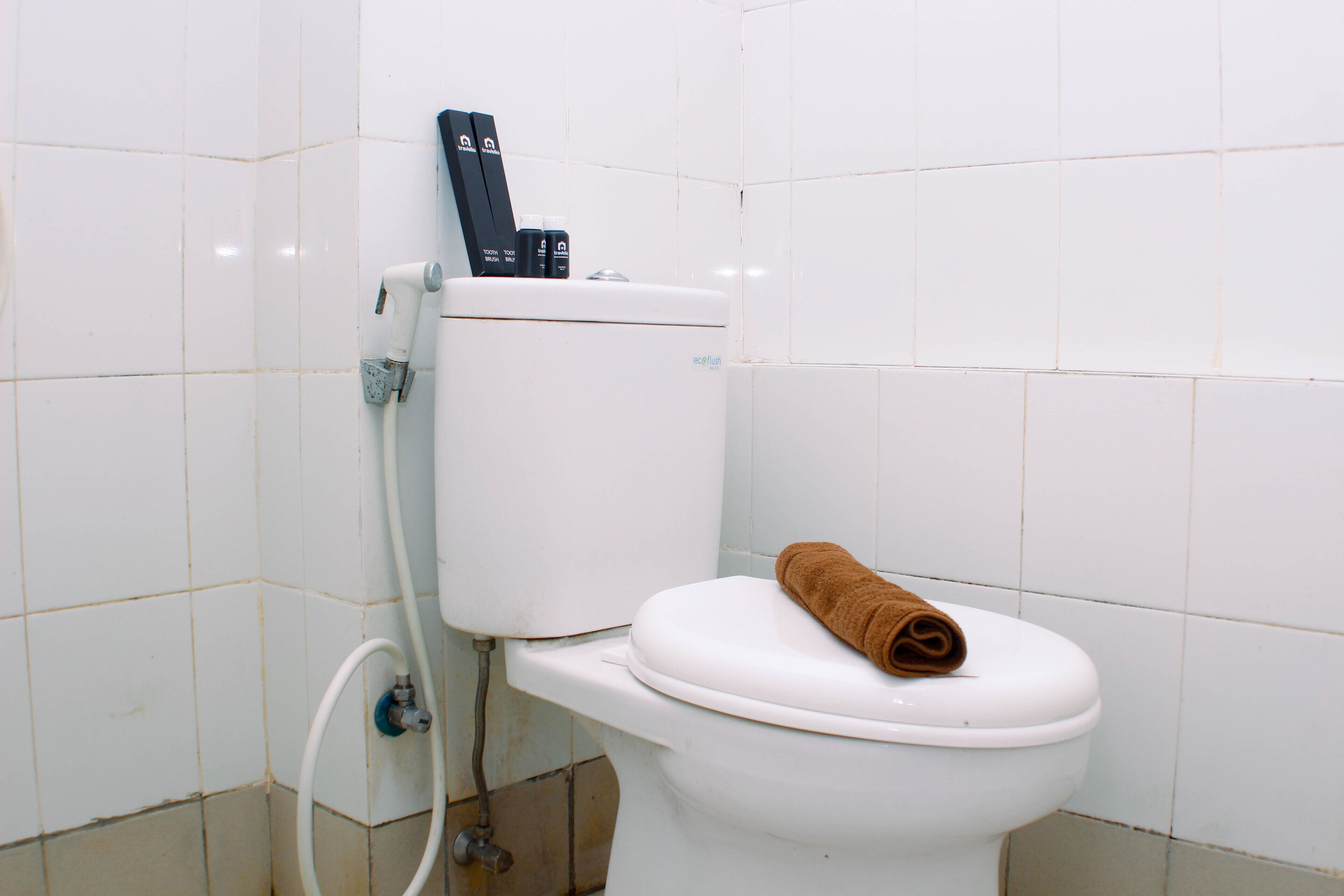 Een wit toilet met een bruine handdoek op de bril en een douchetje.