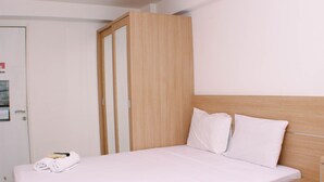 Une chambre d’hôtel avec un lit, une armoire en bois, une table de chevet et une serviette sur le lit.