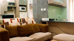 A living room with a sofa, ottoman, and a remote control on a table. - Nice And Best Deal 2Br At Green Pramuka City Apartment (Jakarta)