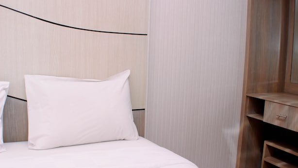 A neatly made bed with white bedding and a single white pillow in a room with wooden paneling and a wooden cabinet with drawers. - Nice And Best Deal 2Br At Green Pramuka City Apartment (Jakarta)