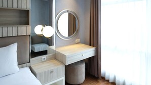 A hotel room with a bed, a vanity with a mirror, a bedside table, and a small stool. - Nice And Relax 1Br At Grand Sungkono Lagoon Apartment (Surabaya)