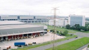 A large industrial building with a loading dock, a parking area, and a tall electricity pylon. - Luxurious Studio At Vasanta Innopark Apartment (Cikarang)