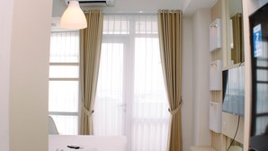 A hotel room with a bed, a desk, a TV, and a window with curtains. - Luxurious Studio At Vasanta Innopark Apartment (Cikarang)