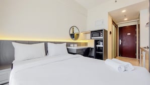A hotel room with a large bed, a desk with a computer, a microwave, and a small seating area. - Studio Room With Simply Look At Sky House Bsd Near Aeon (Pagedangan)