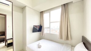 Hotellihuone, jossa on sänky, seinälle asennettu televisio, ikkuna verhoilla ja peili.