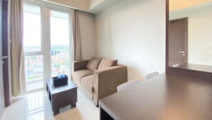 Moderni hotellihuone, jossa on suuri ikkuna, sohva, pieni pöytä ja iso työpöytä.