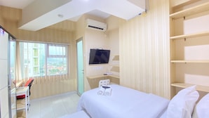 Une chambre d’hôtel équipée d’un lit, d’une télévision, d’un climatiseur, d’un bureau et d’une fenêtre donnant sur des immeubles.