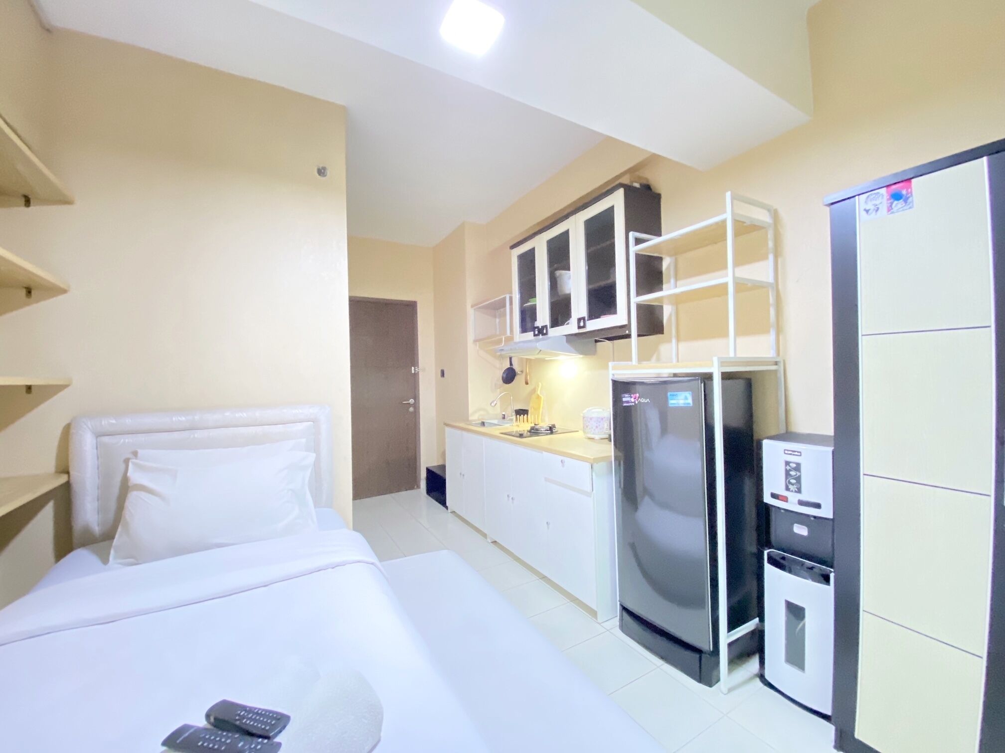 Habitación de hotel con cama, una pequeña kitchenette que incluye un refrigerador, un microondas y un lavamanos. Hay una puerta que conduce a otra habitación.